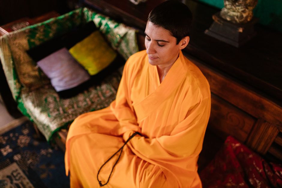 A monk in orange robes meditates indoors, embodying peace and mindfulness.